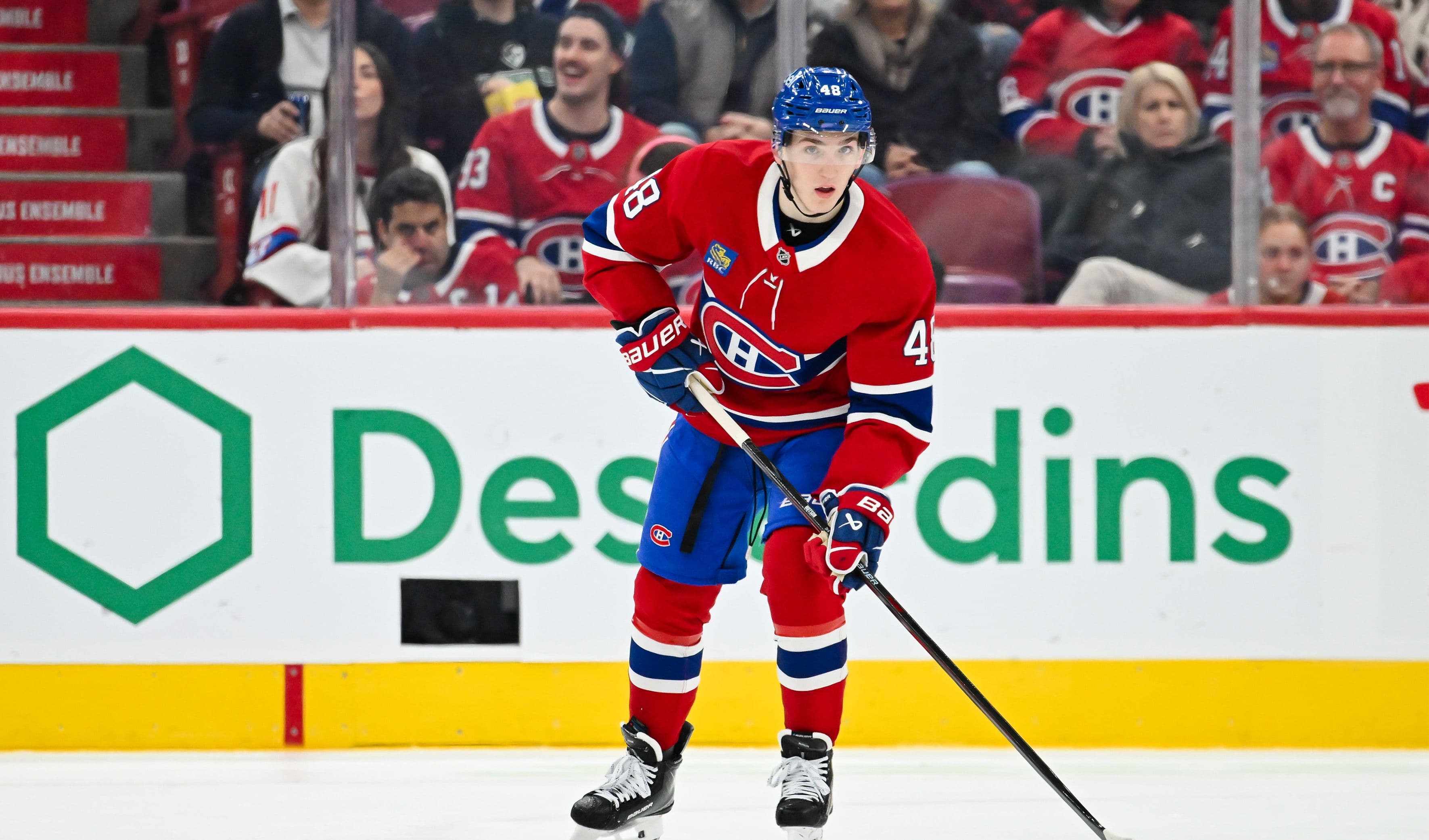 A hockey player in a red jersey with number 43 and a blue helmet skates on an ice rink, holding a stick.