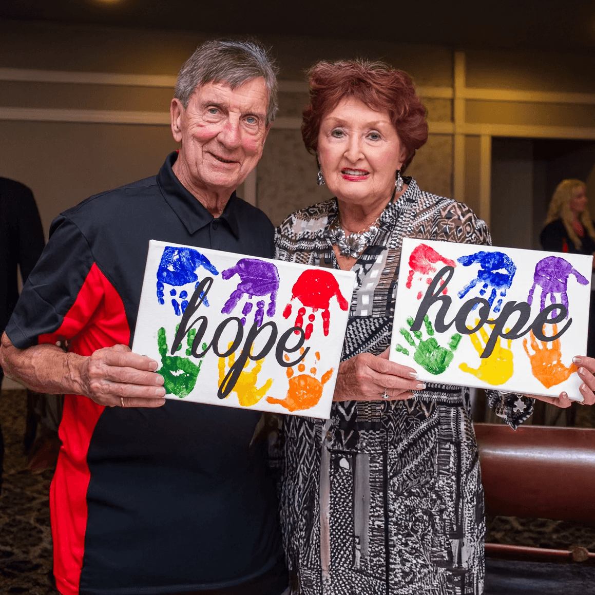 Ted and Joanne Lindsay holding “hope” artwork with handprints.
