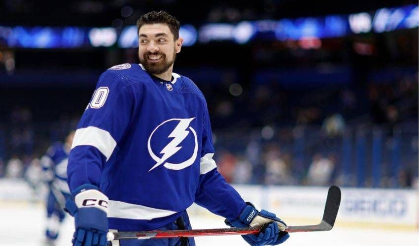 Tampa Bay Lightning player Nick Paul on the ice in full uniform, smiling while holding his stick during warmups.