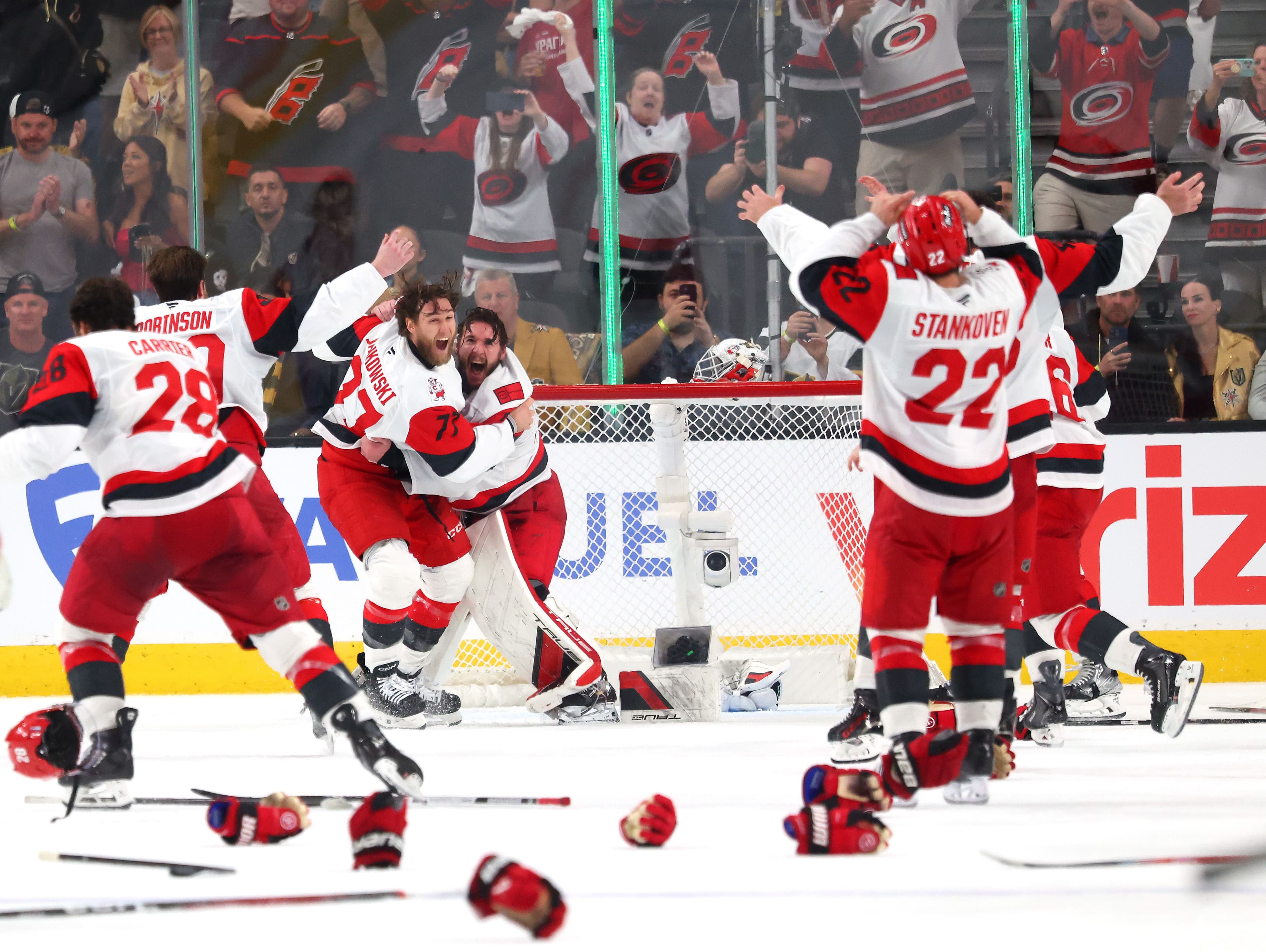 Florida Panthers hockey players celebrate on the ice near the goal as fans cheer in the stands, with discarded gloves and sticks scattered on the rink